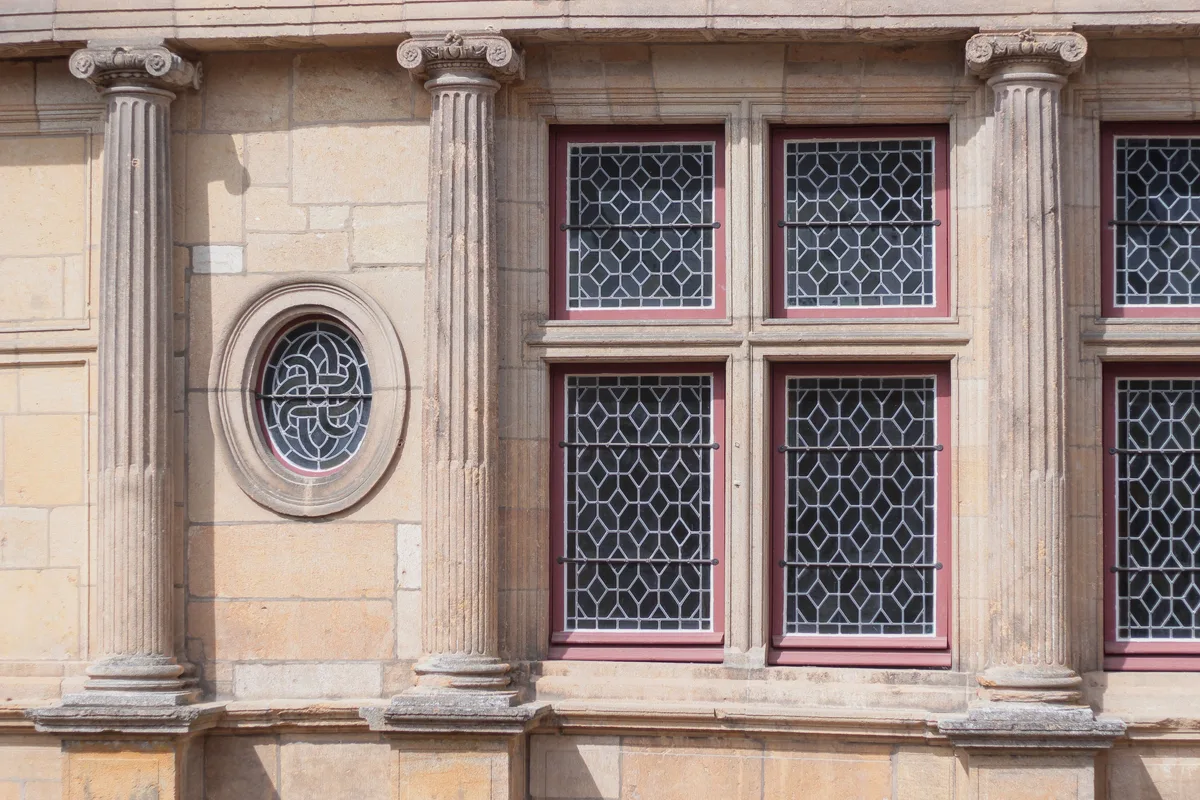 Œil-de-bœuf ovale en pierre sur une façade Renaissance, à côté de fenêtres à petits-bois